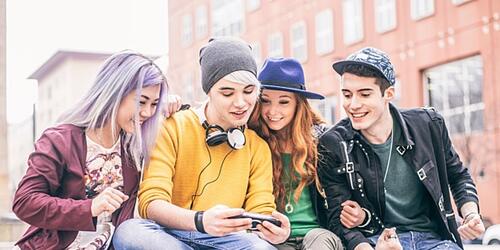 Group of teenagers sit on a wall and look at a phone